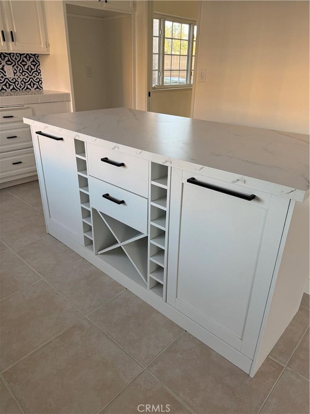 kitchen featuring light stone counters, backsplash, light tile patterned flooring, and white cabinets