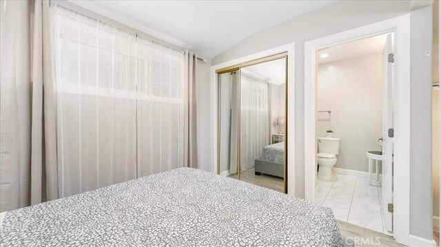 bedroom featuring ensuite bath, vaulted ceiling, and a closet