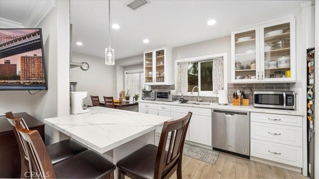 kitchen with decorative light fixtures, white cabinetry, sink, light stone counters, and stainless steel appliances