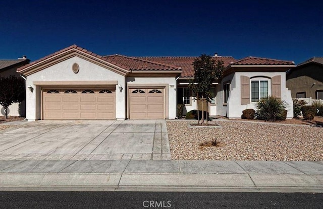 mediterranean / spanish-style house with an attached garage, stucco siding, driveway, and a tiled roof