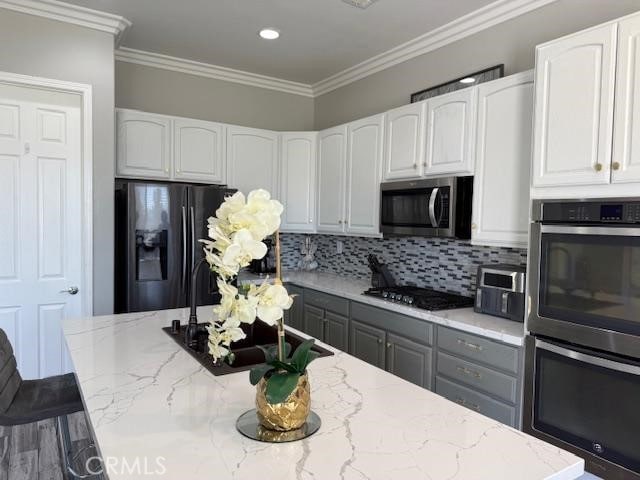 kitchen featuring appliances with stainless steel finishes, ornamental molding, backsplash, and light stone countertops