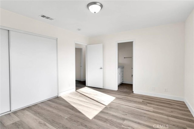 unfurnished bedroom featuring connected bathroom, light wood-type flooring, and a closet