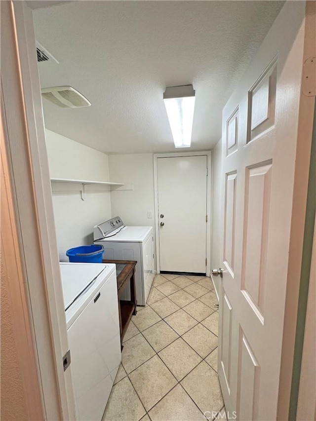 washroom with a textured ceiling, washing machine and clothes dryer, and light tile patterned flooring