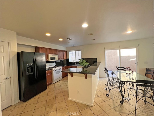 kitchen with a kitchen bar, sink, light tile patterned floors, kitchen peninsula, and white appliances