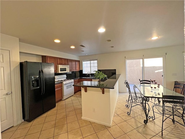 kitchen featuring sink, white appliances, light tile patterned floors, a kitchen breakfast bar, and kitchen peninsula