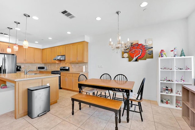 kitchen with light brown cabinetry, gas range oven, a kitchen island with sink, and hanging light fixtures