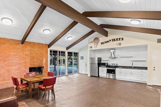 kitchen with sink, wall chimney range hood, appliances with stainless steel finishes, vaulted ceiling with beams, and brick wall