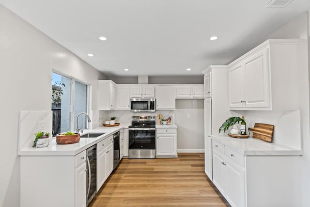 kitchen with appliances with stainless steel finishes, light hardwood / wood-style floors, sink, and white cabinets