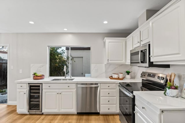 kitchen with sink, appliances with stainless steel finishes, wine cooler, white cabinets, and light wood-type flooring