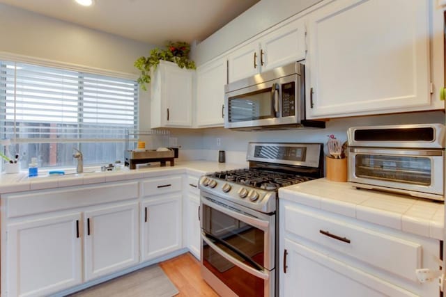 kitchen featuring stainless steel appliances, tile countertops, and white cabinets