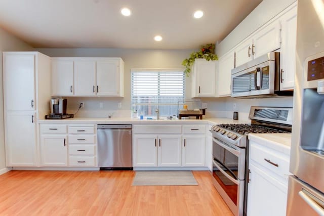 kitchen with sink, stainless steel appliances, white cabinets, tile countertops, and light wood-type flooring