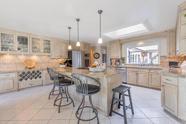 kitchen with light tile patterned floors, stainless steel appliances, a center island, a kitchen bar, and light brown cabinetry