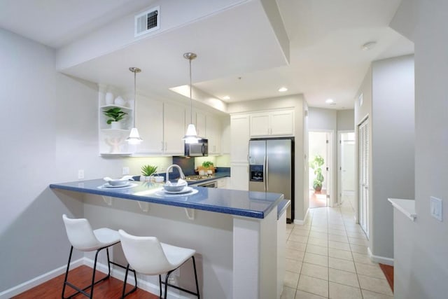 kitchen with pendant lighting, stainless steel appliances, white cabinets, a kitchen bar, and kitchen peninsula