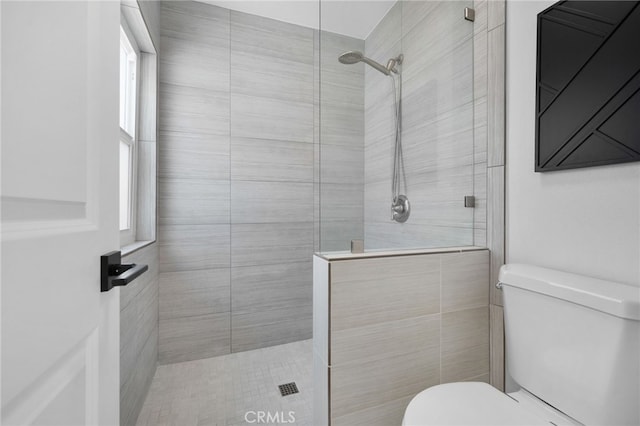 bathroom with a tile shower and toilet