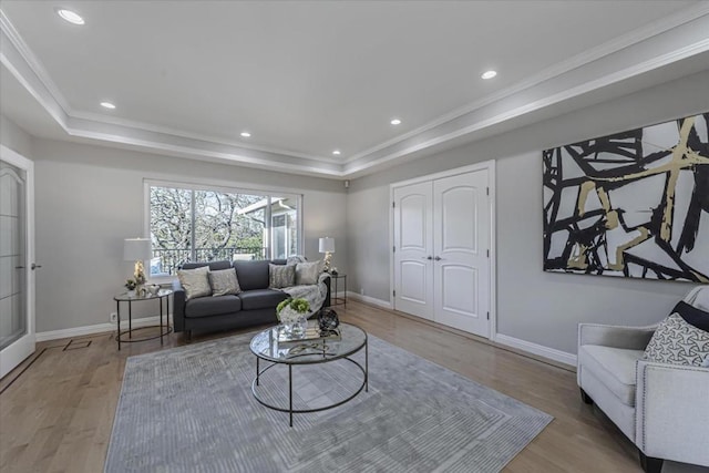 living room with wood-type flooring, ornamental molding, and a tray ceiling