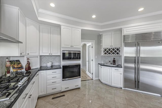 kitchen with stainless steel appliances, white cabinetry, dark stone countertops, and wall chimney exhaust hood