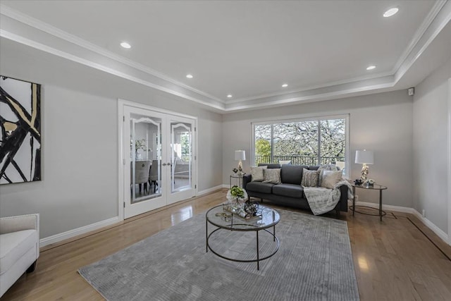 living room featuring crown molding, light hardwood / wood-style flooring, a raised ceiling, and french doors