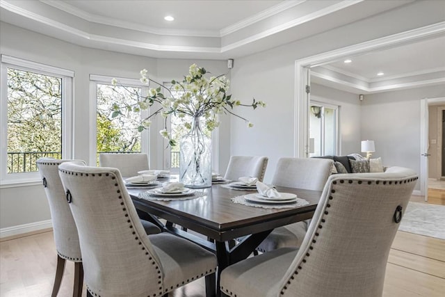 dining space with crown molding, a raised ceiling, light wood-type flooring, and a wealth of natural light