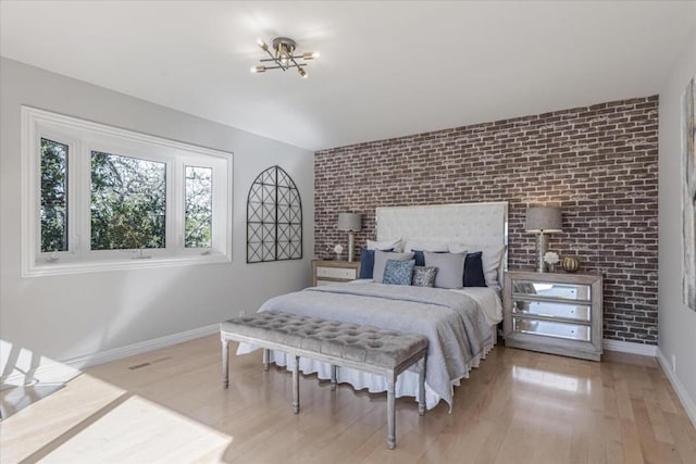 bedroom with brick wall and light hardwood / wood-style floors