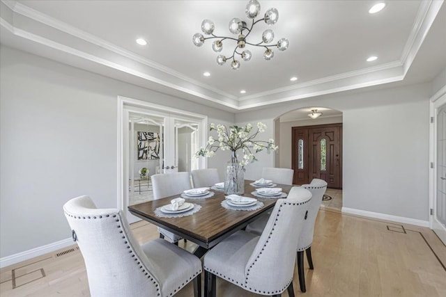 dining space with a raised ceiling, ornamental molding, an inviting chandelier, and light hardwood / wood-style floors