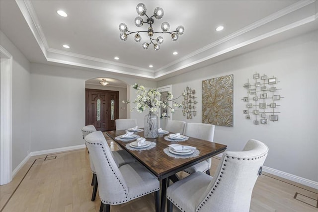 dining room with an inviting chandelier, ornamental molding, a raised ceiling, and light wood-type flooring