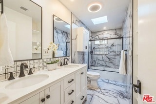 bathroom featuring a skylight, decorative backsplash, vanity, toilet, and a shower with door