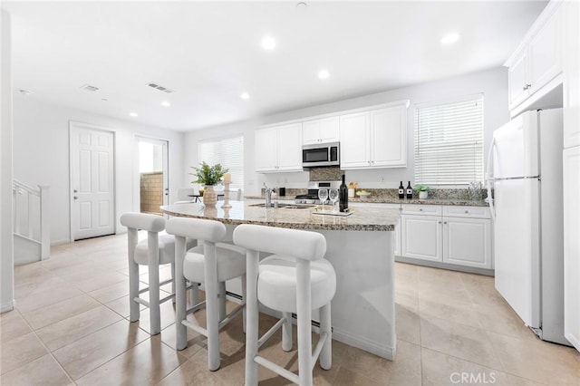 kitchen featuring white cabinetry, a center island with sink, stainless steel appliances, light stone countertops, and light tile patterned flooring