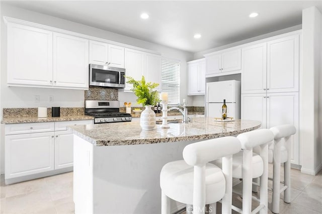 kitchen with white cabinetry, sink, stainless steel appliances, and an island with sink