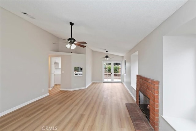 unfurnished living room featuring french doors, vaulted ceiling, a brick fireplace, and light wood-type flooring