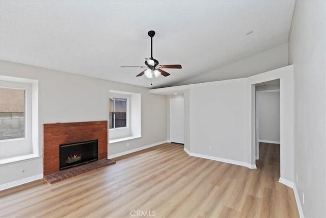 unfurnished living room with ceiling fan, vaulted ceiling, a fireplace, and light wood-type flooring