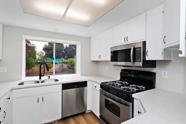 kitchen featuring stainless steel appliances, sink, light hardwood / wood-style flooring, and white cabinets