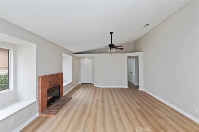 unfurnished living room with ceiling fan, lofted ceiling, a fireplace, and light wood-type flooring