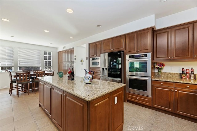 kitchen with light tile patterned floors, a kitchen island, light stone countertops, and appliances with stainless steel finishes