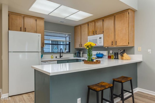 kitchen featuring sink, a kitchen bar, light hardwood / wood-style floors, kitchen peninsula, and white appliances