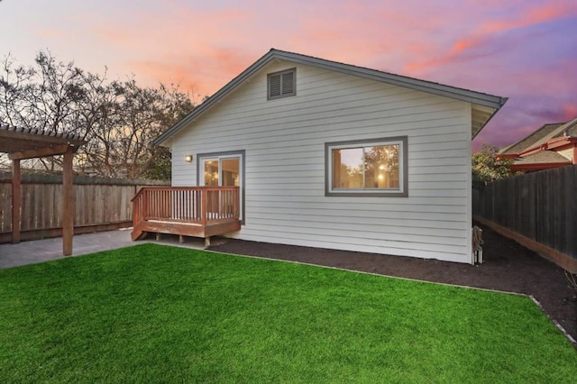 back house at dusk with a pergola, a deck, and a lawn