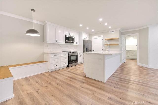 kitchen featuring sink, white cabinets, hanging light fixtures, stainless steel appliances, and a center island with sink