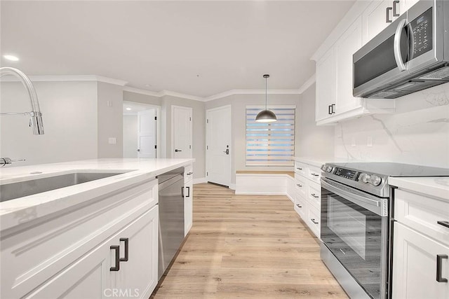 kitchen featuring appliances with stainless steel finishes, pendant lighting, white cabinetry, light stone counters, and light hardwood / wood-style floors