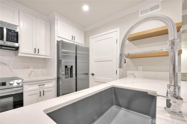 kitchen featuring light stone countertops, appliances with stainless steel finishes, ornamental molding, and white cabinets