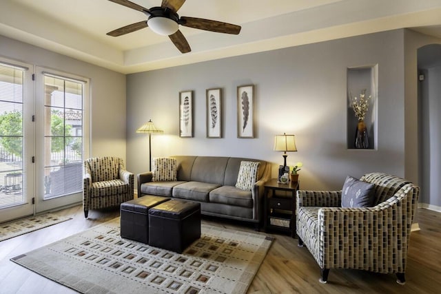 living room with a raised ceiling, hardwood / wood-style floors, and ceiling fan