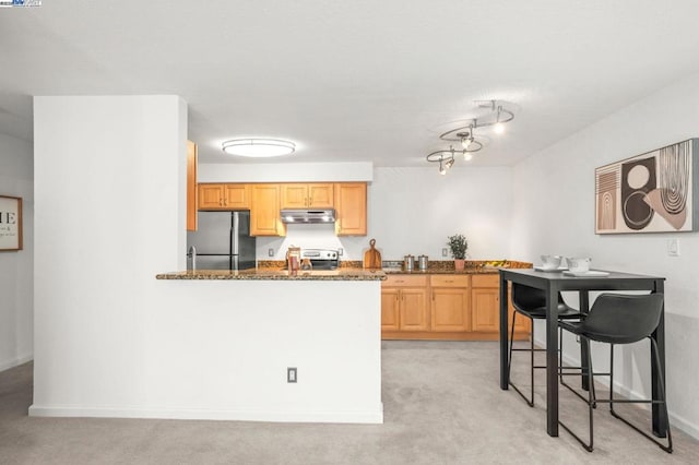 kitchen with dark stone countertops, stainless steel appliances, light brown cabinetry, light colored carpet, and kitchen peninsula