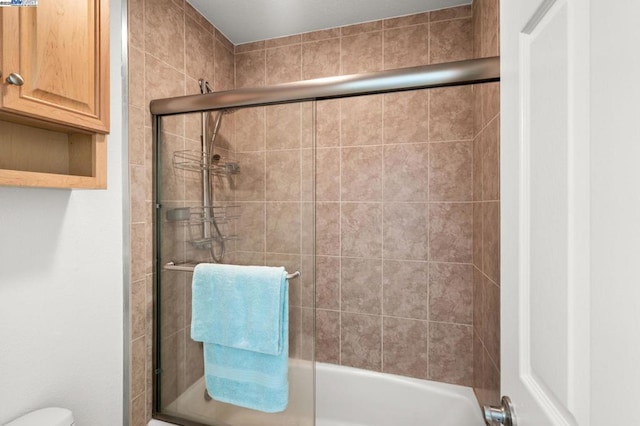 bathroom featuring combined bath / shower with glass door and toilet