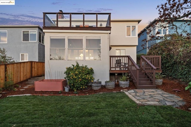 back house at dusk featuring a yard and a balcony