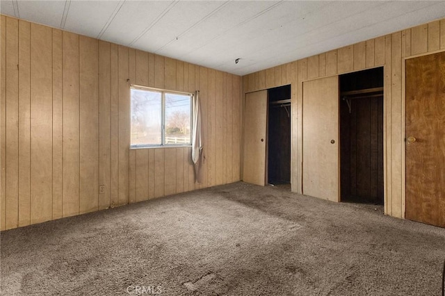 unfurnished bedroom featuring carpet floors, two closets, and wood walls