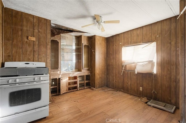 kitchen with ceiling fan, wood walls, light wood-type flooring, and gas range gas stove