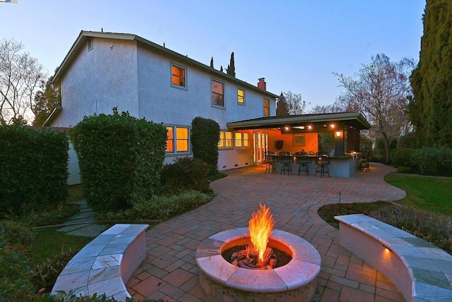 back house at dusk featuring a patio, exterior bar, and a fire pit