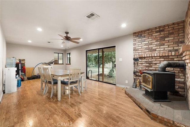 dining room with ceiling fan, light hardwood / wood-style flooring, and a wood stove