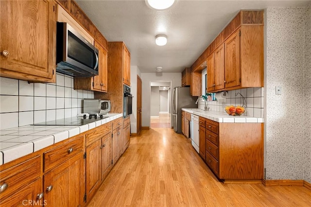 kitchen with sink, tile counters, light hardwood / wood-style floors, and black appliances