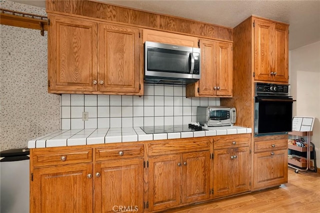 kitchen featuring backsplash, tile countertops, black appliances, and light wood-type flooring