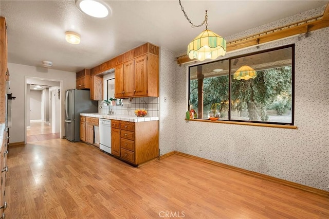 kitchen featuring decorative light fixtures, light hardwood / wood-style flooring, stainless steel refrigerator, dishwasher, and oven