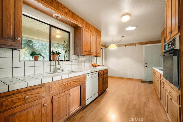 kitchen featuring sink, tile countertops, white dishwasher, pendant lighting, and wall oven